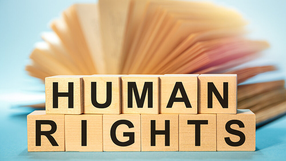 Wooden letter cubes form the words ‘HUMAN RIGHTS’ against a fanned out, blurred book background.