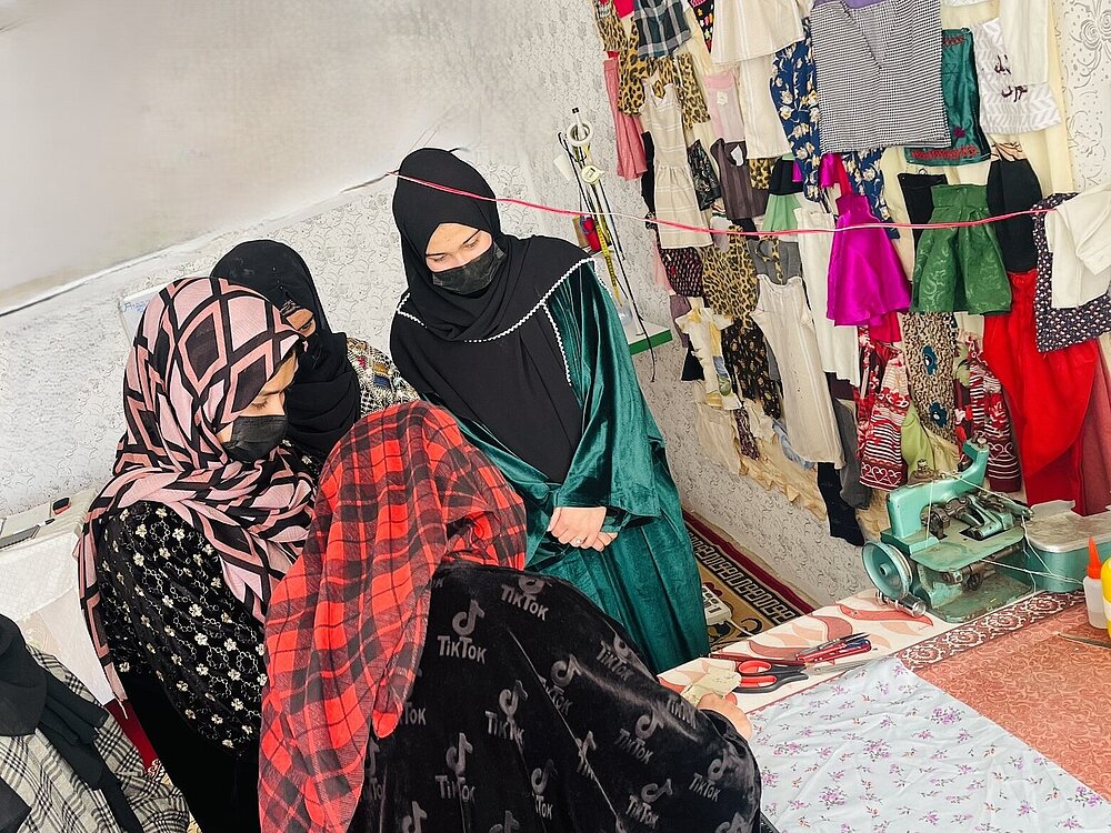 Drei Afghanische Unternehmerinnen sitzen zwischen Stoffen zusammen.