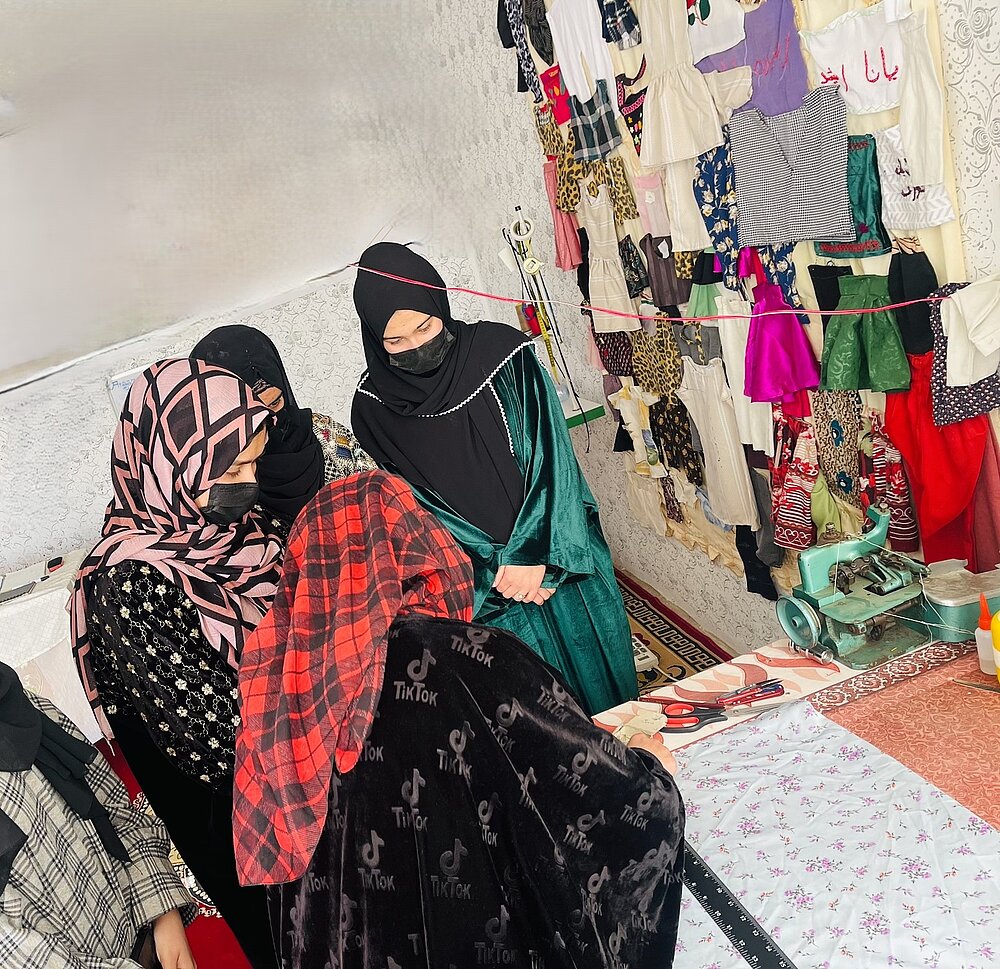 Drei Afghanische Unternehmerinnen sitzen zwischen Stoffen zusammen.